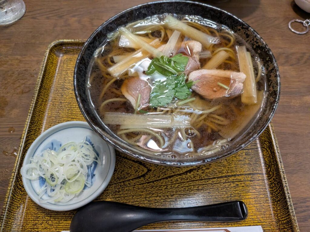 千葉の街を歩いていると、ふと入りたくなる昔ながらの蕎麦屋がある。
千葉市中央区にある「阿づ満庵 本店」。
葭川公園駅から歩いてすぐ、千葉銀座の一角に店を構える老舗です。店内もどこか懐かしく、今の街の風景の中に昔ながらの蕎麦屋の空気が残っています。阿づ満庵 本店
今回いただいたのは、温かい「鴨南ばん」。
鴨の旨みが溶け込んだ、温かいそば
温かいそばの中でも、鴨南ばんは少し特別な存在。
鴨肉の旨みと、出汁の効いたつゆ。
そこに蕎麦が合わさり、冷えた体をゆっくり温めてくれます。
阿づ満庵 本店では、鴨南ばんのほかにも、天ぷらそばや親子南ばん、カレー南ばん、おかめなど、昔ながらの蕎麦屋らしい温かいメニューが並びます。
なかでも鴨南ばんは、店の定番として長く親しまれている一品。
茶蕎麦で味わう、阿づ満庵らしさ
阿づ満庵の蕎麦は、緑がかった茶蕎麦が特徴。
細めの蕎麦を温かいつゆと一緒にすすると、鴨の旨みと蕎麦の風味が口の中に広がります。
派手さのある一杯ではない。
けれど、こういう蕎麦がいい。
街を歩いて、暖簾をくぐって、温かいそばを一杯。
そんな時間そのものまで含めて楽しみたくなる店です。
千葉の街に残る、昔ながらの蕎麦屋
阿づ満庵 本店は、JR千葉駅からも徒歩圏内。
葭川公園駅からは徒歩約2分ほどとアクセスもよく、千葉市美術館や千葉銀座周辺を歩く途中にも立ち寄りやすい場所です。
最近は、新しいカフェやレストランを目的に街を歩くことが多い。
でも、こうした昔から続く店を訪ねてみるのも面白い。
新しいものと、ずっと変わらないもの。
その両方があるから、街歩きは楽しい。
阿づ満庵 本店の鴨南ばんは、そんなことを思わせてくれる一杯でした。